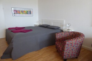 A bedroom with a bed, pillows, a chair, a bedside table, and a wall decoration. - Holiday apartment with 2 bedrooms (Fehmarn)