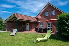 A brick house with a covered patio, a lawn chair, a table, and a red umbrella. - Holiday home with 3 bedrooms (Schönberger Strand)