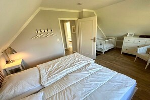 A bedroom with a bed, a crib, a dresser, and a door leading to another room. - Holiday home with 3 bedrooms (Schönberger Strand)