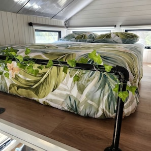 En seng med blomstret dyne og en sort metalgavl med slyngplanter.