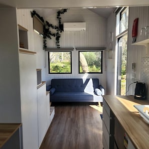 A compact living space with a sofa, a coffee machine, and a window overlooking greenery.