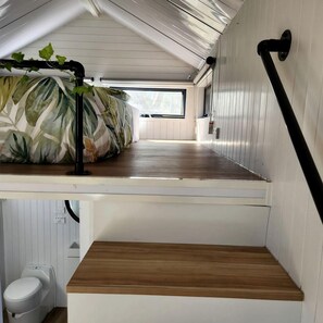 A compact room with a bed, a small window, and a white toilet.