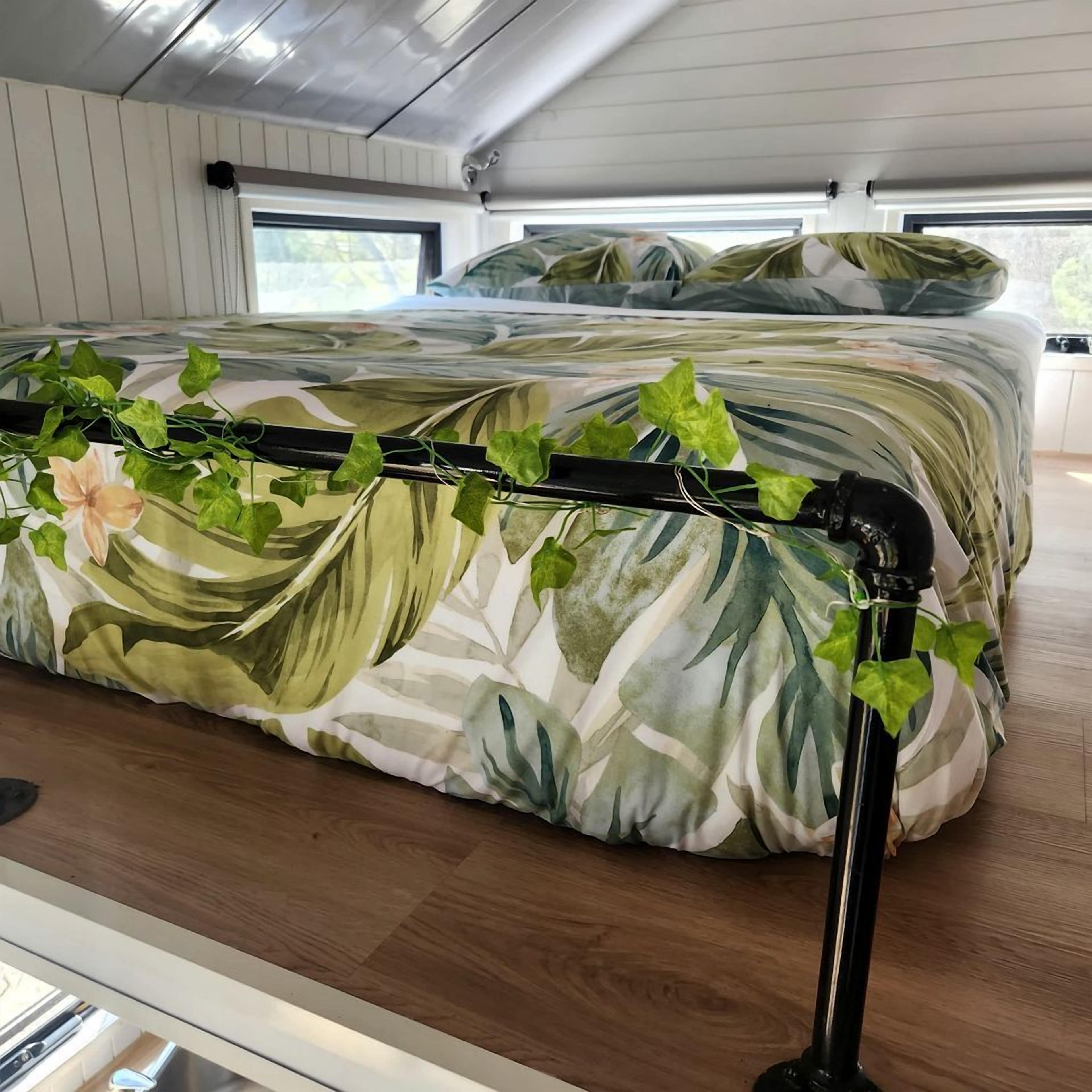 Una cama con cubrecama floral y cabecera metálica negra con enredaderas.