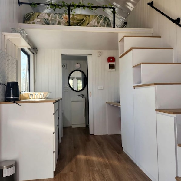 A compact kitchen with a coffee maker, a sink, and a mirror.
