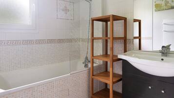 Une salle de bain avec une baignoire, une étagère en bois et un lavabo.
