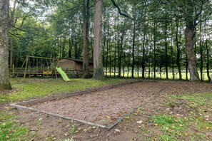 Zona boscosa amb un parc infantil, que inclou cadira d'oscalls i tobogan, i una petita construcció de fusta.