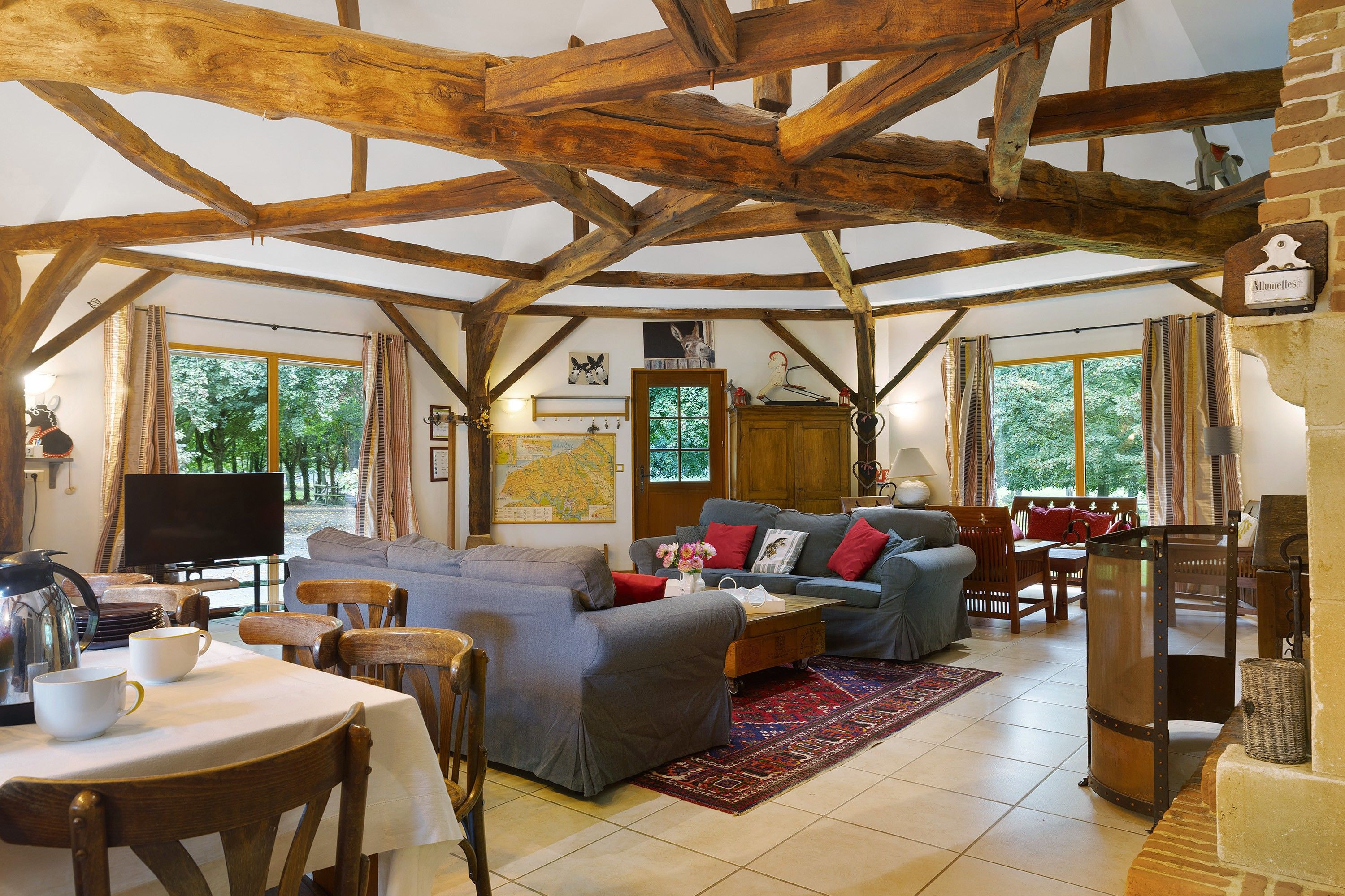 A rustic interior with exposed wooden beams, a dining area with a table and chairs, and a living room with sofas and a television.