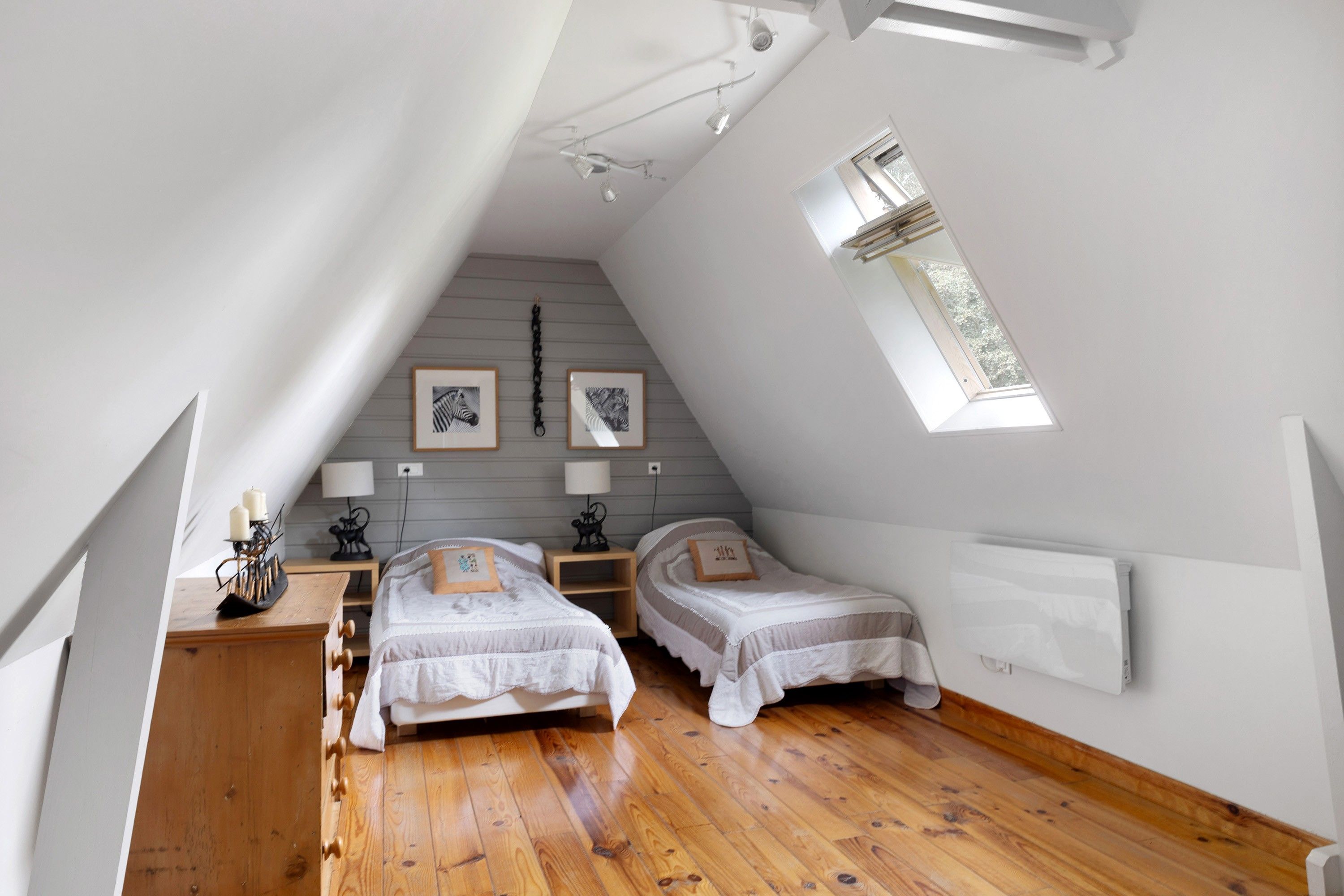 Een slaapkamer met twee bedden, een houten dressoir, een bureau en een dakraam.