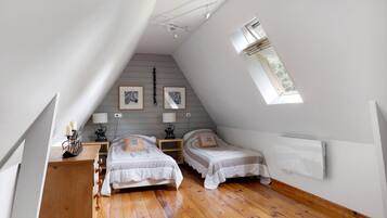 Een slaapkamer met twee bedden, een houten dressoir, een bureau en een dakraam.