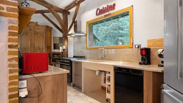 Eine Küche mit Holzbalkendecke, einem roten Herd, einer Kaffeemaschine und einem Schild mit der Aufschrift 'Cuisine'.