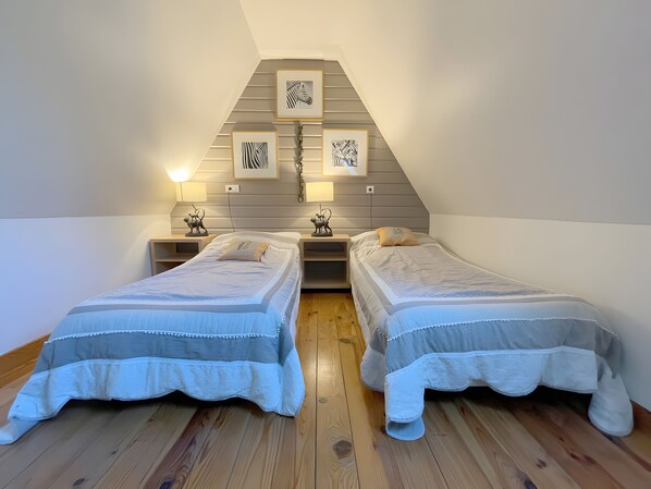 Une chambre avec deux lits, un plancher en bois et des œuvres d’art accrochées au mur.