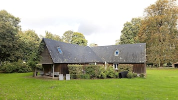 Ein rustikales Bauernhaus mit geneigtem Dach, einer Veranda mit Sitzgelegenheit und einem grünen Feld im Vordergrund.