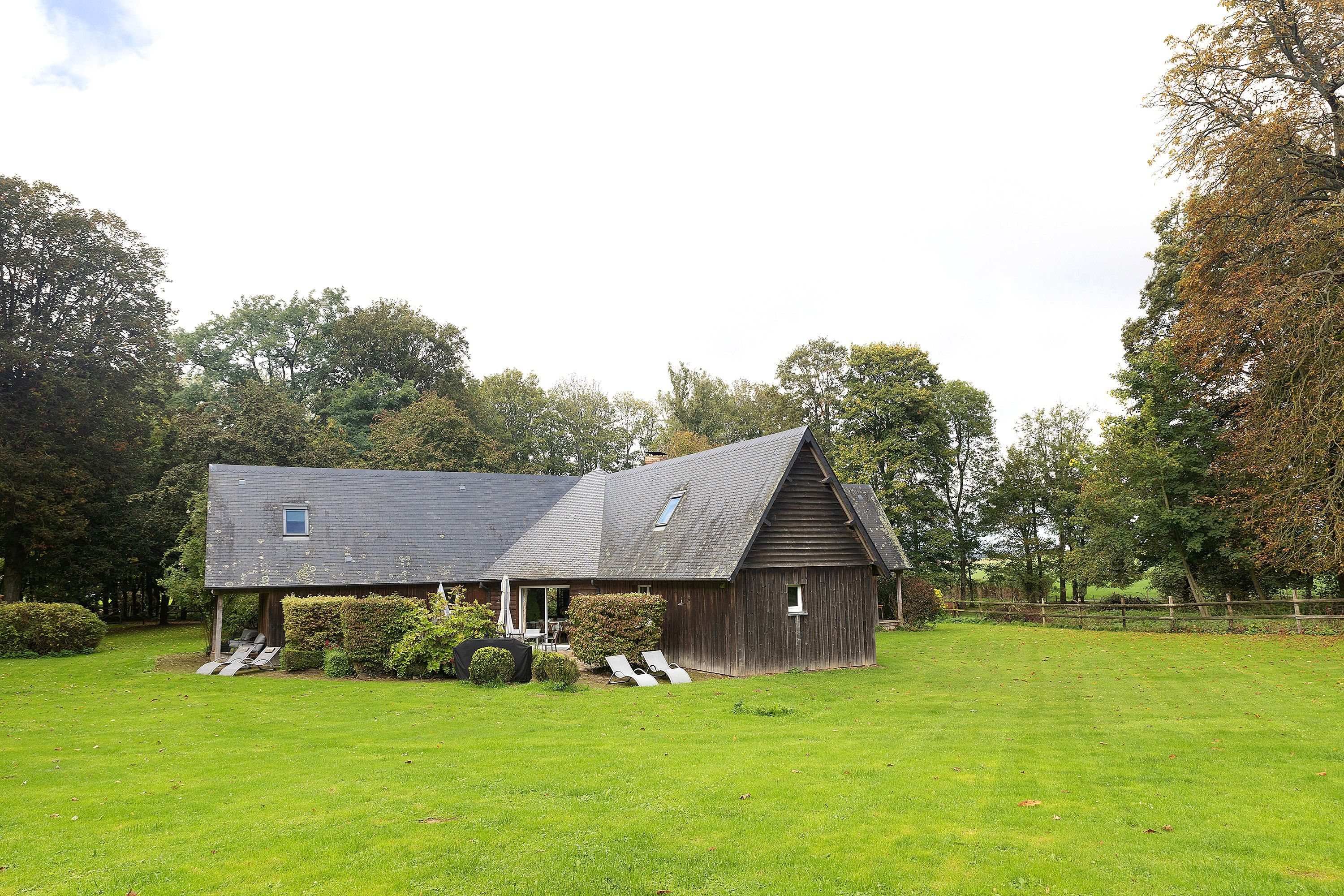 A wooden barn with a sloped roof, surrounded by a grassy field and trees.
