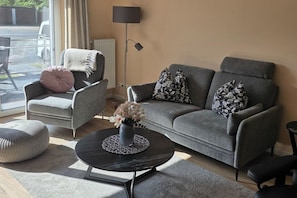 Una sala de estar moderna con un sofá gris, una mesa redonda de centro y un sillón con cojín.