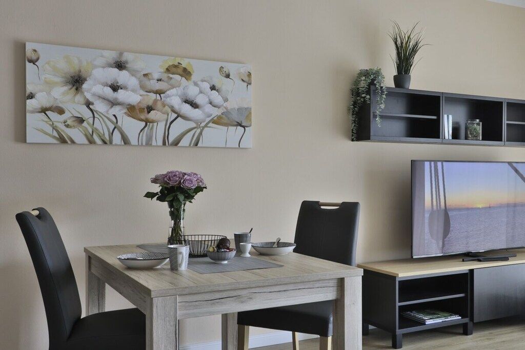 A dining area with a wooden table, black chairs, a vase with flowers, and a painting on the wall.
