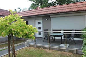 A residential building with a red-tiled roof, a white door, and a covered patio area with a table and chairs. - Holiday apartment Ostseewoge (Ostseebad Nienhagen)