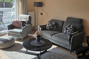 A modern living room with a grey sofa, a round coffee table, and a grey armchair. - Holiday apartment Ostseewoge (Ostseebad Nienhagen)