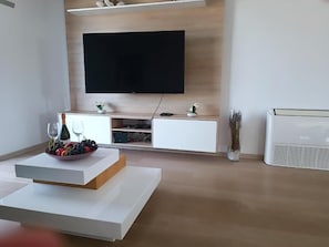 Ein modernes Wohnzimmer mit einem an einer Holzwand montierten Flachbildfernseher, einer weißen Unterhaltungsanlage mit einer Glasvase und einem weißen Couchtisch mit einer Obstschale.