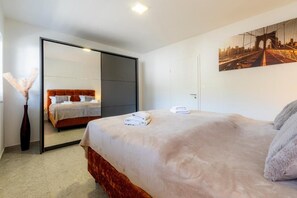 Ein Hotelzimmer mit einem Bett, einem großen Spiegel, einem Bild an der Wand und einer Vase mit Pampasgras.