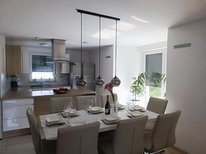 Een moderne keuken met een eethoek, met een centraal kookeiland, hanglampen en uitzicht op de omgeving.