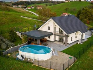 Een huis met een zwembad, een overdekt terras en een omheind gazon.