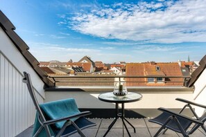 Een balkon met een tafel en stoelen, met uitzicht op een woonwijk met rode dakpannen.