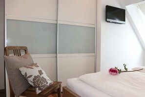 Een slaapkamer met een bed, een stoel met kussen, een aan de muur bevestigde televisie en een raam.