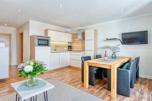 Een moderne keuken met een inbouwoven, een eettafel met stoelen en een flatscreen televisie aan de muur.