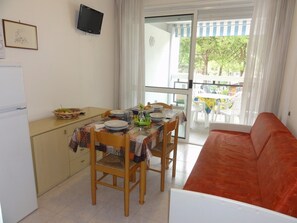 Ein Essbereich mit einem Tisch für vier Personen, einer Couch, einem an der Wand befestigten Fernseher und Blick auf den Balkon.