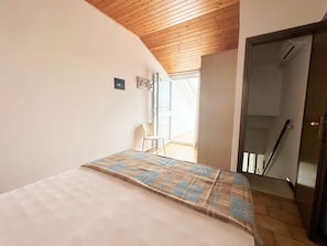 Ein Schlafzimmer mit Bett, Stuhl, Holzboden und einer Tür zum Balkon.