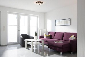 A modern living room with a white sofa, a black armchair, and a white coffee table. - Seilerstr./Knyphausenstr.26A - Fiene (Norderney)