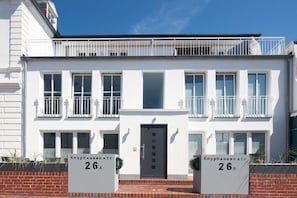 A two-story building with a balcony on the upper floor, a black door, and two signs indicating the address 'Knyphausenstr. 26A' and 'Knyphausenstr. 26B'. - Seilerstr./Knyphausenstr.26A - Fiene (Norderney)