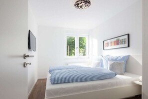 A bedroom with a bed, a window, a door, and a wall-mounted TV. - Seilerstr./Knyphausenstr.26A - Fiene (Norderney)