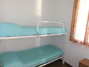 Un lit superposé à deux niveaux, une fenêtre avec des rideaux et une petite table en bois.