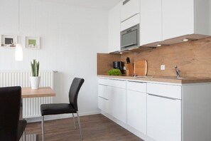 Eine moderne Küche mit weißen Schränken, einer Holz Arbeitsplatte, einem schwarzen Stuhl und einem Topf mit Pflanze.