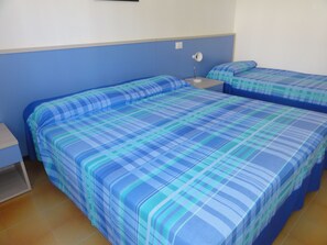 A room with two beds, each with blue and green checkered bedding. There is a nightstand with a lamp between the beds. - Charming terraced villa (Bibione)