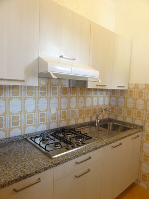 A kitchen with a gas stove, stainless steel sink, and white cabinets. - Charming terraced villa (Bibione)