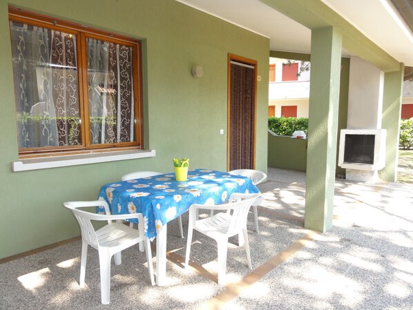 A patio with a table and chairs, a window with curtains, and a door. - Charming terraced villa (Bibione)