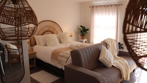 Een slaapkamer met een bed, nachtkastjes, een bank, een hanglamp, een potplant en een raam met gordijnen.