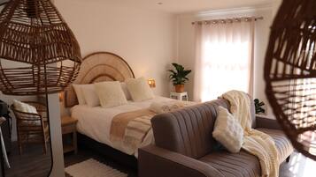 A bedroom with a bed, bedside tables, a sofa, a hanging light, a potted plant, and a window with curtains.