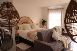 A bedroom with a bed, bedside tables, a sofa, a hanging light, a potted plant, and a window with curtains. - Studio 304 @ The Majestic: One Bedroom Apartment (Cape Town)