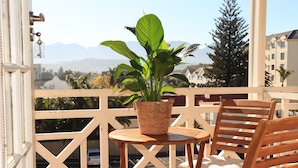 Een balkon met een houten stoel, een tafeltje en een potplant.