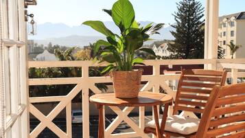 Een balkon met een houten stoel, een tafeltje en een potplant.
