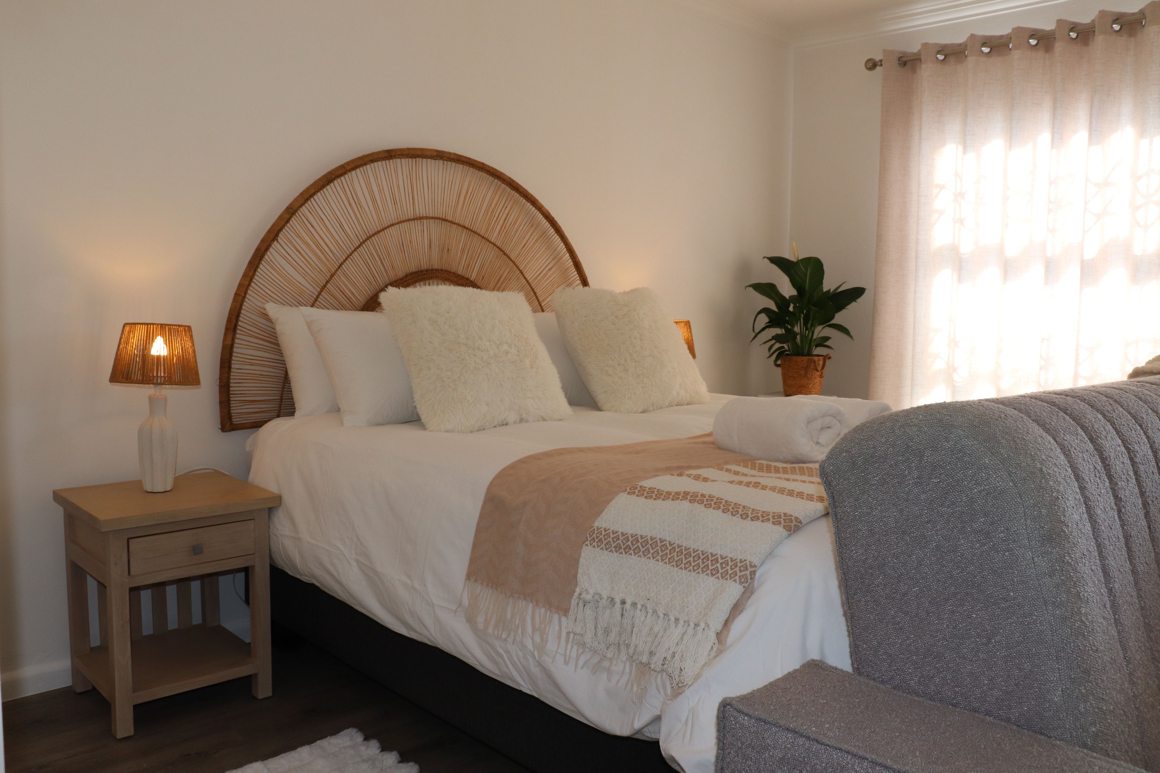 A bedroom with a bed, bedside table, lamp, potted plant, and a window with curtains.