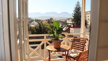 Een balkon met uitzicht op bergen, een bloempot en twee houten stoelen.