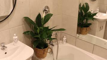 A bathroom with a bathtub, a sink, a mirror, and a potted plant.