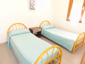 Una habitación con dos camas individuales de estructura metálica amarilla, una mesita de noche pequeña y un cuadro colgado en la pared.