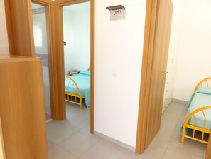 Une pièce comprenant un lit, un bureau et une chaise. Une porte donne accès à une autre pièce.