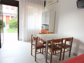A dining area with a white table and wooden chairs, a microwave, and a cabinet. - Ground-floor flat with garden (Bibione)