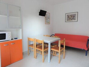 Une pièce de taille modeste, avec une table blanche, quatre chaises en bois, un canapé rouge, un four à micro-ondes et un petit meuble.